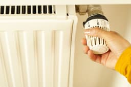 O mână care reglează un robinet termostatat de calorifer